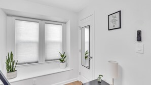 A modern room with a large window, a mirror, a framed picture, a remote control, and a small plant on the windowsill.