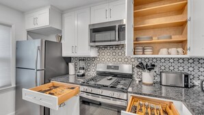 A modern kitchen with white cabinets, a stainless steel refrigerator, a microwave, a stove, and a toaster.