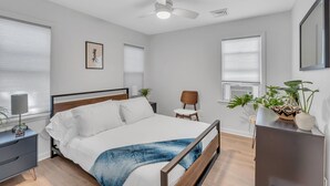 A modern bedroom with a bed, bedside table, chair, and a ceiling fan.