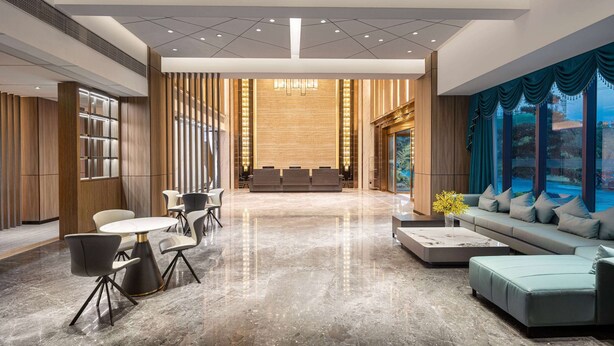 Un lobby moderno con mostrador de recepción, zona de estar y ventanas grandes con cortinas.