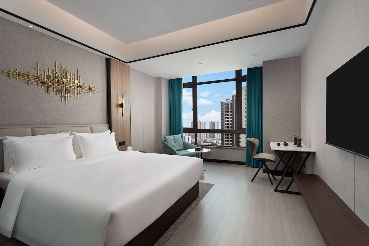 Quarto de hotel moderno com uma cama grande, uma escrivaninha e vista para a cidade.