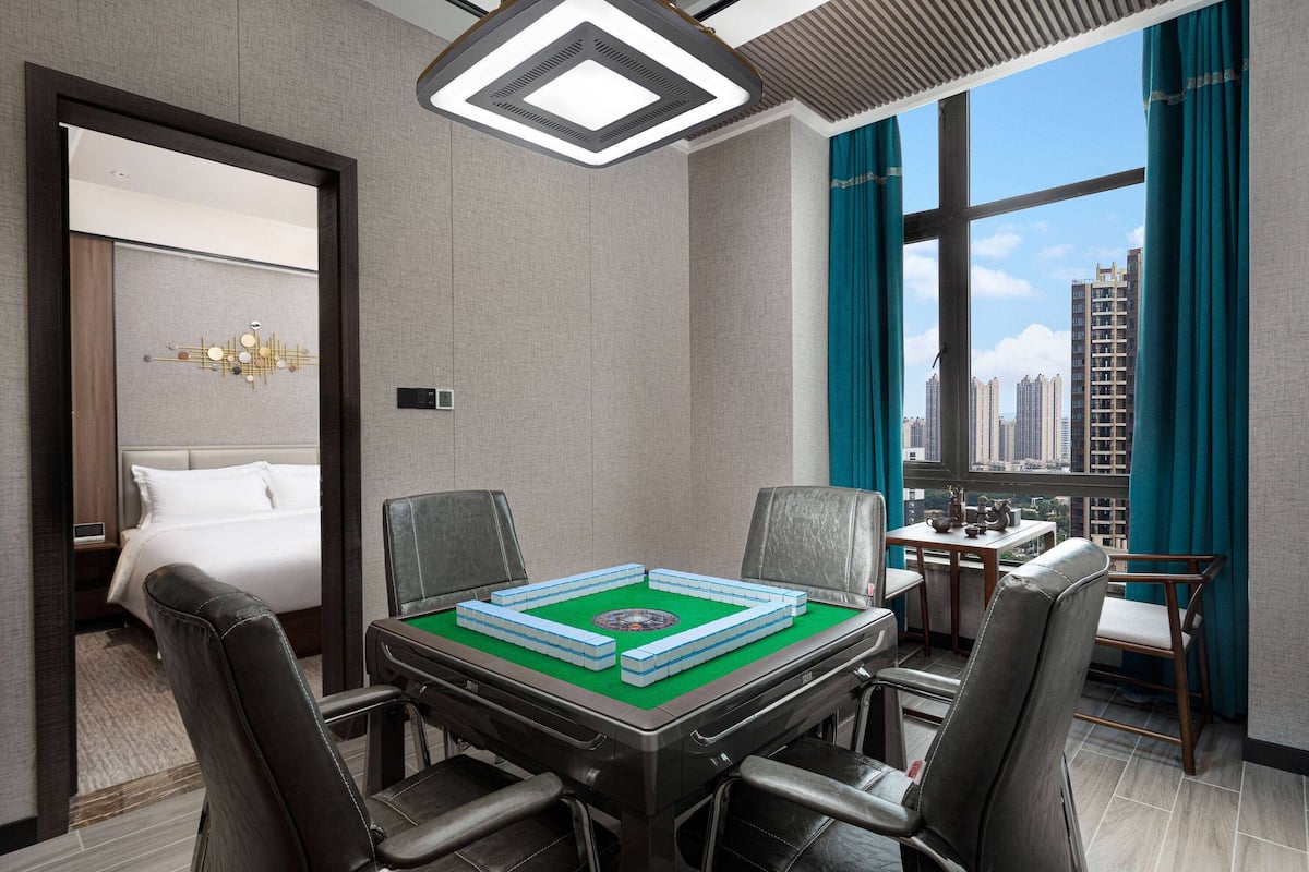 Quarto de hotel com cama, mesa de jantar com cadeiras, mesa de bilhar e vista para a cidade.