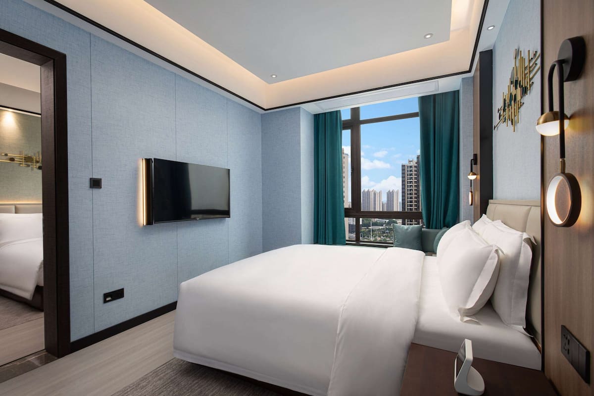 Quarto de hotel moderno com uma cama grande, televisão de tela plana, vista para a cidade e decoração minimalista.