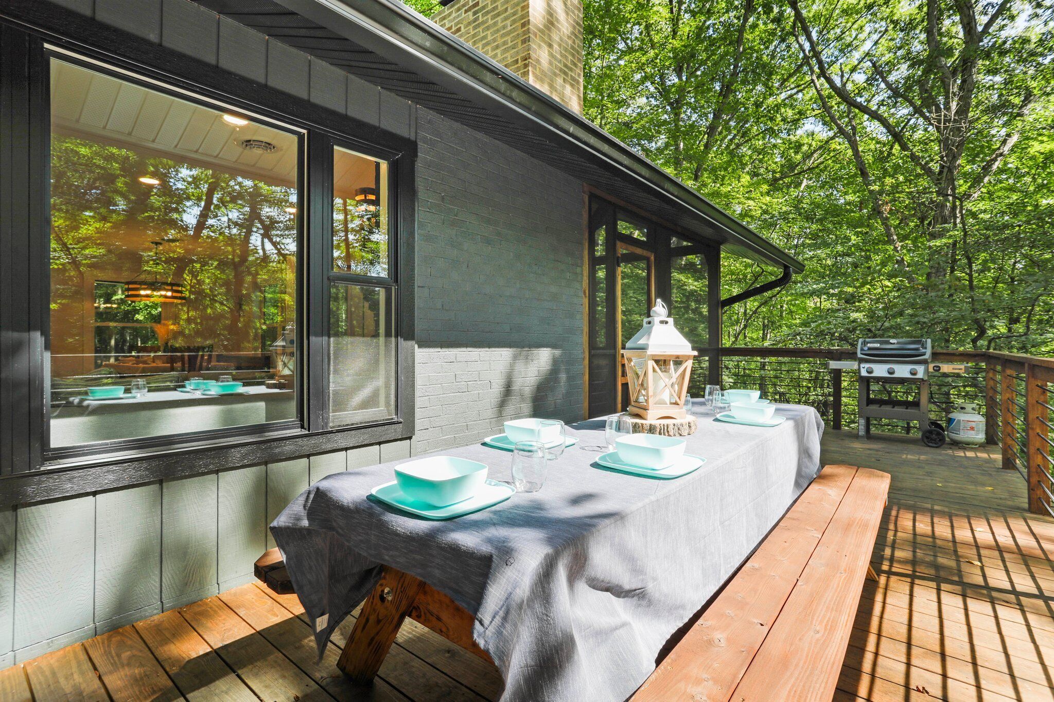 An outdoor dining area with a table set for two, a lantern, and a grill.