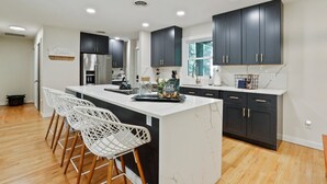 A modern kitchen with dark cabinets, a white island, and bar stools. - 🌻Have FUN in the Fall Foliage TREETOPS🍁Luxury 4 Suite Cabin🍁Screened Porches🌻 (Berkeley Springs)