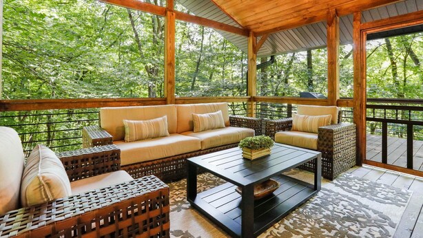 A covered outdoor seating area with a sofa, wicker chairs, and a coffee table. - 🌻Have FUN in the Fall Foliage TREETOPS🍁Luxury 4 Suite Cabin🍁Screened Porches🌻 (Berkeley Springs)