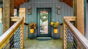 A wooden staircase leading to a dark green door with a wreath, two potted plants, and a welcome sign. - 🌻Have FUN in the Fall Foliage TREETOPS🍁Luxury 4 Suite Cabin🍁Screened Porches🌻 (Berkeley Springs)