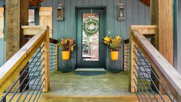 A wooden staircase leading to a dark green door with a wreath, two potted plants, and a welcome sign.