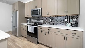 A modern kitchen with beige cabinets, a stainless steel refrigerator, a microwave, a stove, and a coffee maker. - 2 King BR I Front Street + Walk DT (Traverse City)