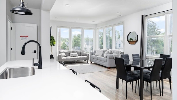 A modern kitchen with a white countertop, black faucet, and a dining area with black chairs and a glass table. - 2 King BR I Front Street + Walk DT (Traverse City)
