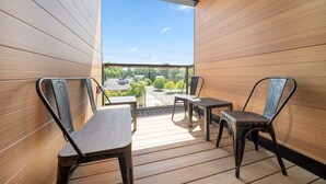 Ein Balkon mit Holzboden und Metallstühlen, mit Blick auf einen Parkplatz und Grünflächen.
