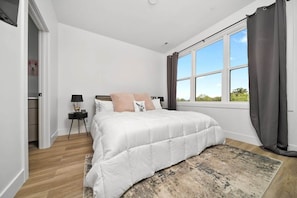 Un dormitorio con una cama grande, una mesita de noche, una ventana con cortinas y vistas a zonas verdes.