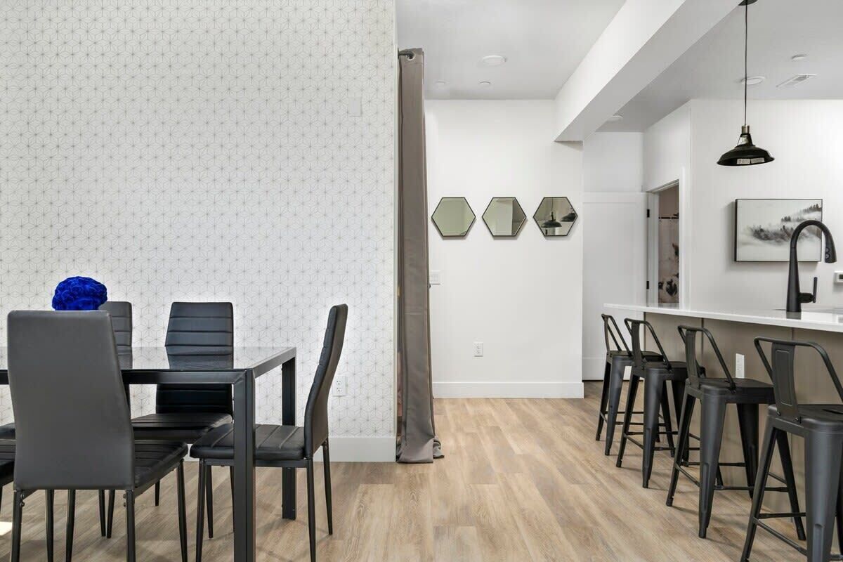 A modern kitchen with a dining area, featuring a wooden floor, black chairs, and a white backsplash.