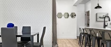 A modern kitchen with a dining area, featuring a wooden floor, black chairs, and a white backsplash.