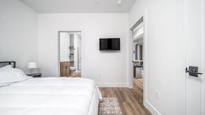 A modern hotel room with a large bed, a flat-screen TV mounted on the wall, and a wooden floor. - Spacious Condo I Front St + 2 King BR I Near DT (Traverse City)