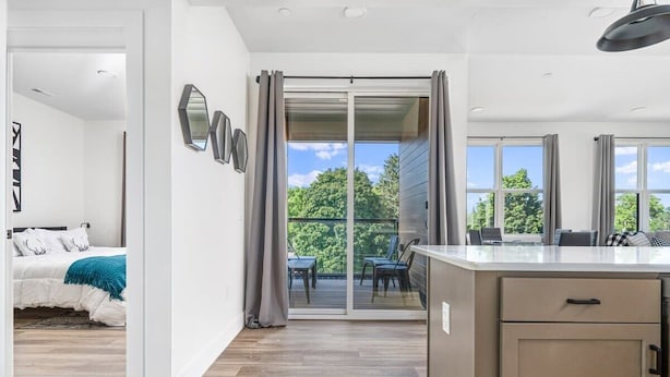 A modern kitchen with a large island, sliding glass doors to a balcony, and a view of greenery. - Spacious Condo I Front St + 2 King BR I Near DT (Traverse City)