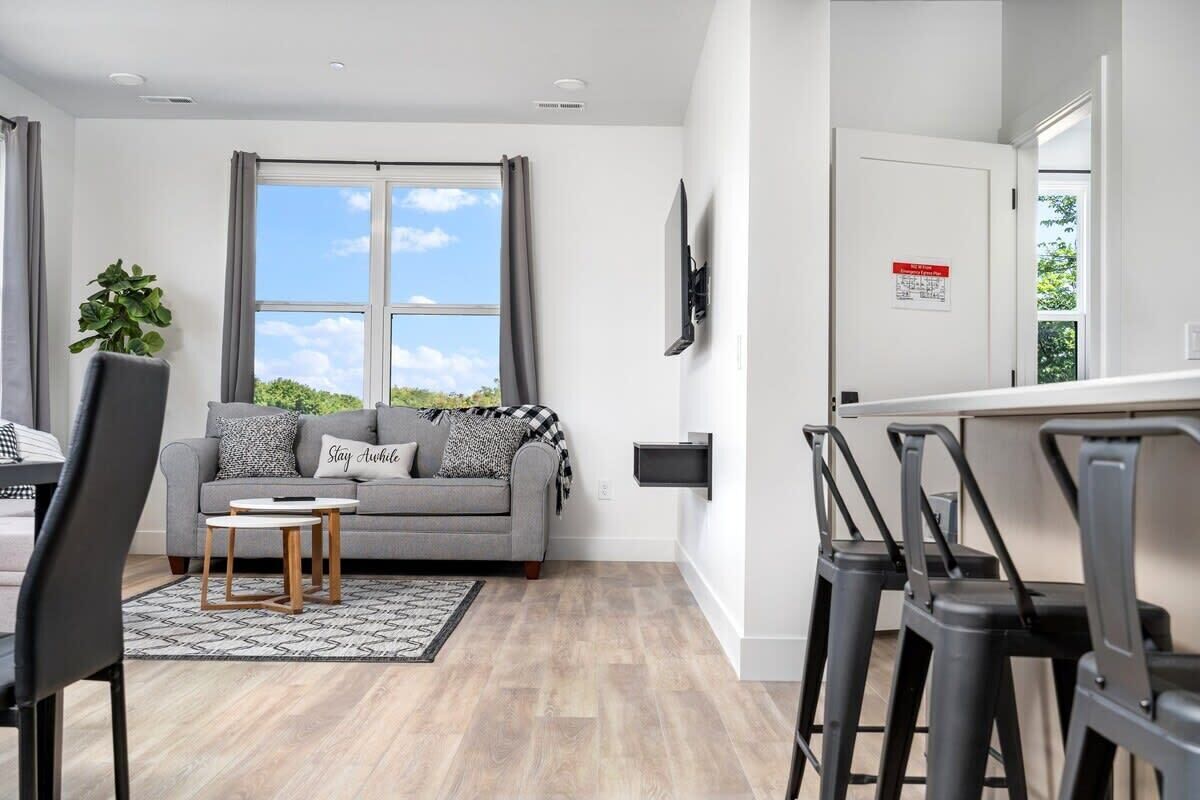 A modern living room with a grey sofa, a small wooden coffee table, and a large window with curtains.