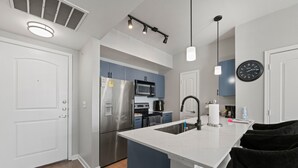 Une cuisine moderne avec des meubles blancs, des appareils en acier inoxydable et des luminaires suspendus.