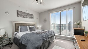 Une chambre moderne avec un grand lit, un ventilateur de plafond, une vue sur la ville et un balcon avec une balustrade.