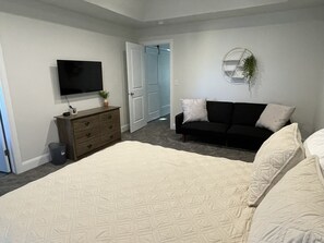 Een slaapkamer met een bed, een kaptafel, een televisie en een deur naar een andere kamer.