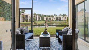 A patio with wicker furniture and a vase, overlooking a building complex and a pond. - Limited-Time Summer Deal on Lovely 2BR Condo with Tennis (naples)