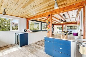 Eine moderne Küche mit Holzbalken, einer blauen Kochinsel und Blick ins Freie.
