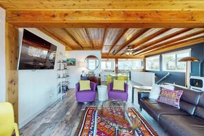 A spacious living area with wooden beams, a sofa, chairs, a glass coffee table, and a colorful rug. - A Serene Waterfront Sanctuary with 360° Views (Bainbridge Island)