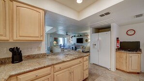 Una cocina con encimeras de granito, armarios de madera, un refrigerador y un televisor sobre un atril de madera.