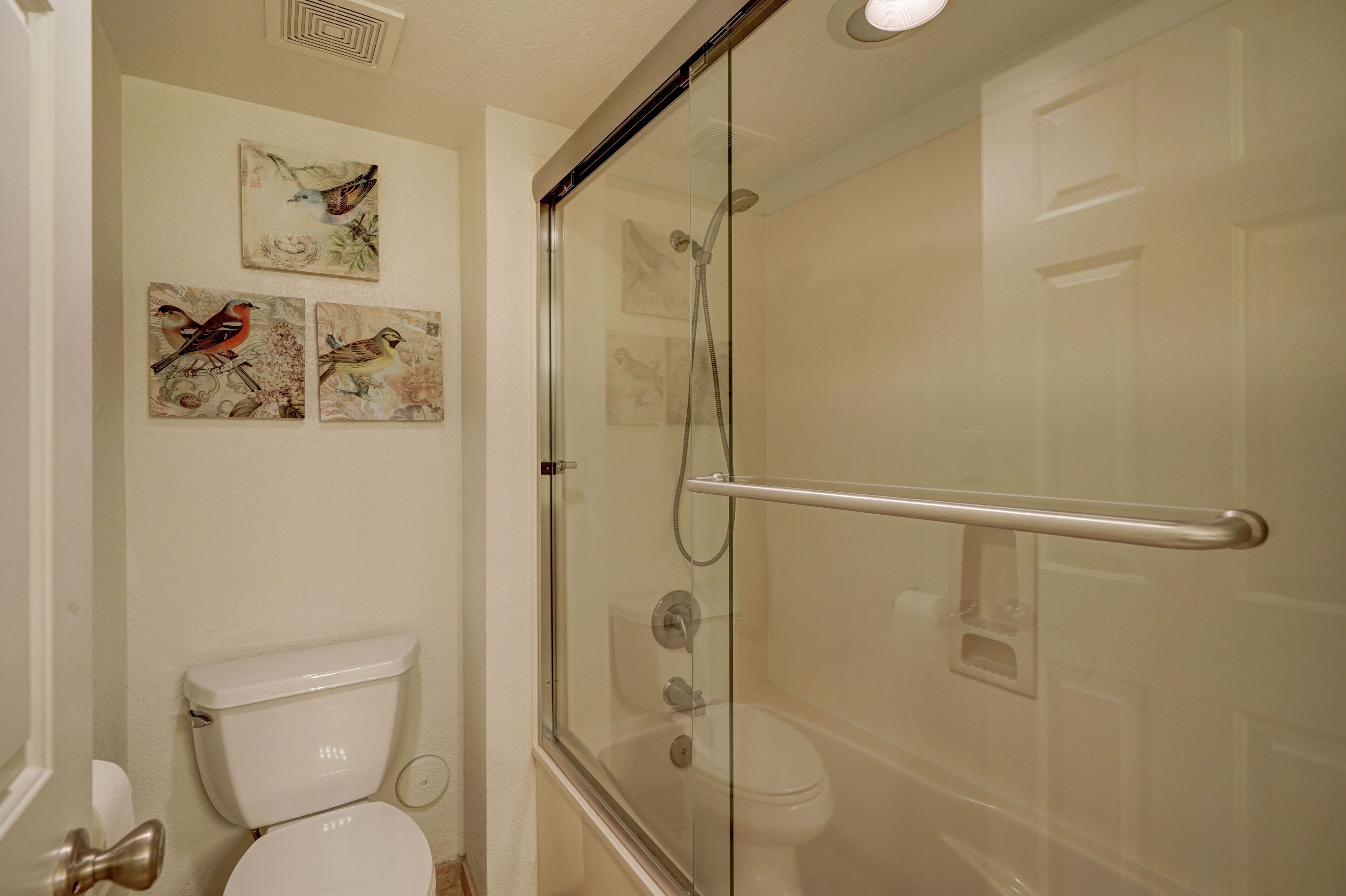 A bathroom with a glass-enclosed shower, a white toilet, and three bird-themed wall art pieces.