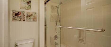 A bathroom with a glass-enclosed shower, a white toilet, and three bird-themed wall art pieces.
