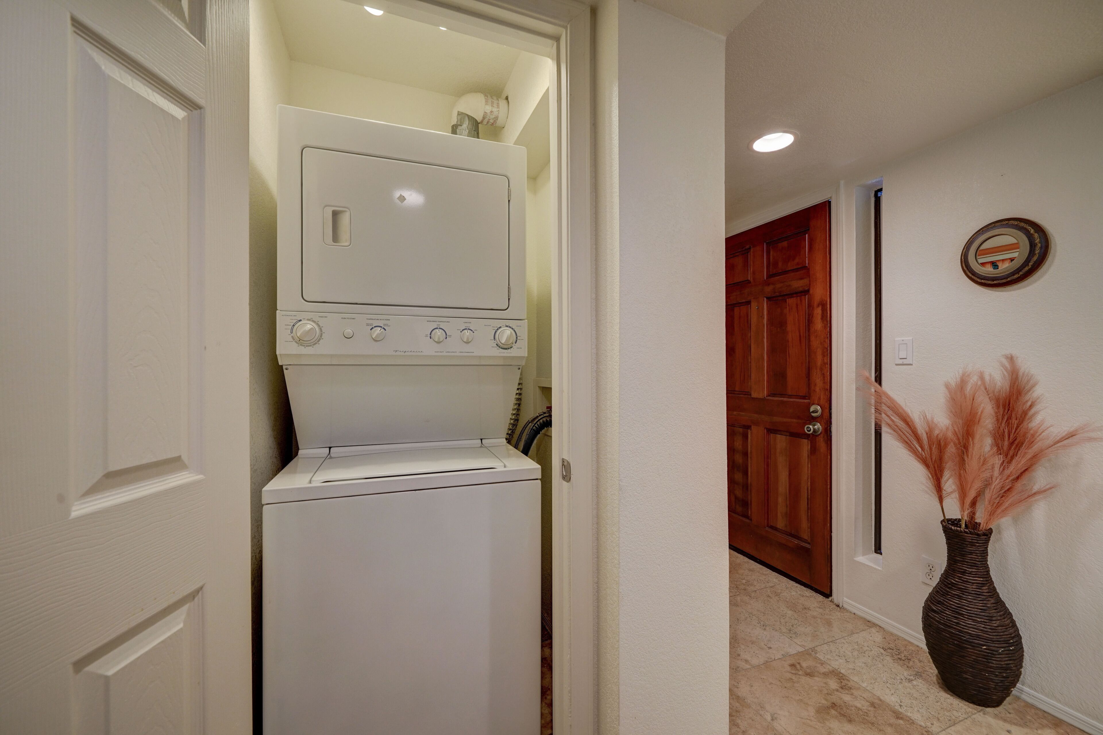 A laundry room with a washer and dryer, a wooden door, and a vase with pampas grass on the floor.