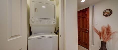 A laundry room with a washer and dryer, a wooden door, and a vase with pampas grass on the floor.