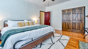 A bedroom with a bed, wooden floor, a ceiling fan, a large wooden door, and a nightstand with a lamp. - Huge 6Bd House Historic Updated King Bed Shaw (St. Louis)