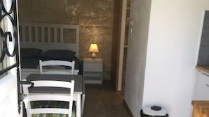 A compact room with a bed, a small table with a lamp, a chair, a trash bin, and a wooden cabinet. - Coquet Studio CDG , Parc Astérix (Coye-la-Forêt)