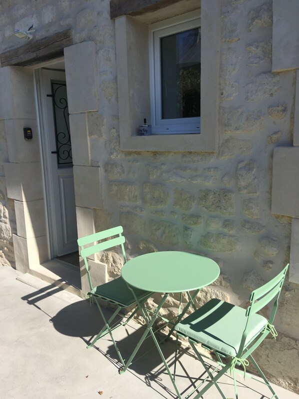 A stone building with a small window, a door, and a table with two chairs.