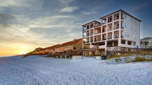 Un hotel frente a la playa con varios pisos, balcones y una escalera de madera que da a la playa.