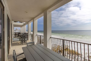 A covered outdoor area with a table and chairs, overlooking a beach with a railing.