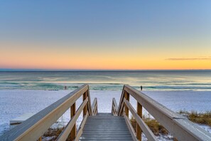 A wooden boardwalk leading to a beach with a clear view of the ocean and a sunset in the background. - Beaux Soleil - Stunning & Modern Beachfront Luxury Home! (Destin)