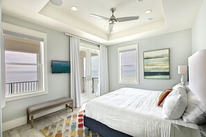 A bedroom with a large bed, a ceiling fan, and a view of the sea through the windows. - Beaux Soleil - Stunning & Modern Beachfront Luxury Home! (Destin)