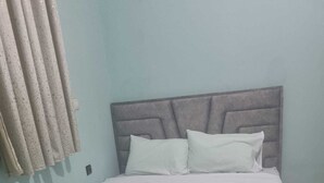Un lit avec une tête de lit grise, une literie blanche et un mur bleu clair.