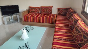 Un salon avec un canapé, un téléviseur posé sur un meuble et une table sur laquelle se trouve une boîte de mouchoirs.