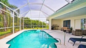 Une piscine dotée d’une structure en verre, entourée de chaises longues et d’un espace barbecue.