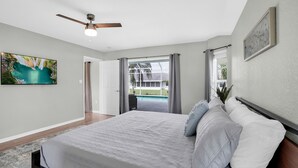 Une chambre avec un lit, un ventilateur de plafond, un tableau et une vue sur une piscine.