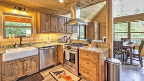 Cocina de cabaña de madera con una isla central, electrodomésticos de acero inoxidable y un amplio ventanal con vistas al bosque.