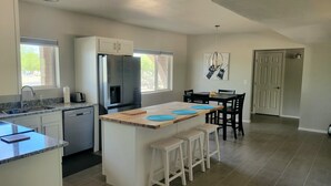 Une cuisine moderne dotée d’un îlot central, de meubles blancs, d’un réfrigérateur en acier inoxydable et d’un coin repas avec une table et des chaises.