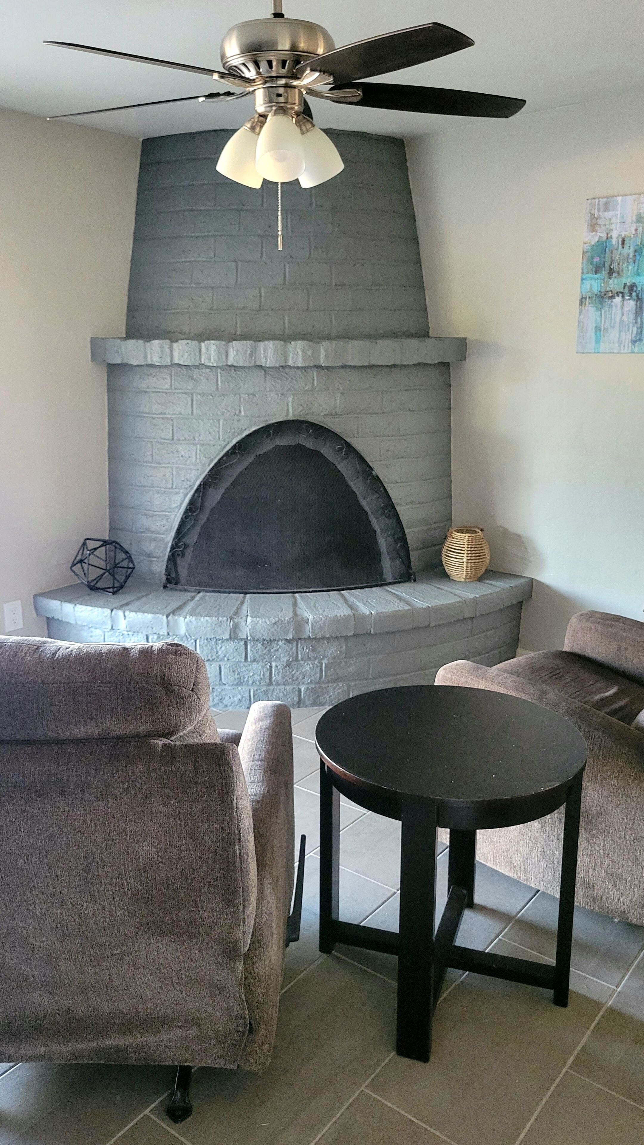 Un salon avec une cheminée, deux fauteuils, une table ronde et un ventilateur de plafond.