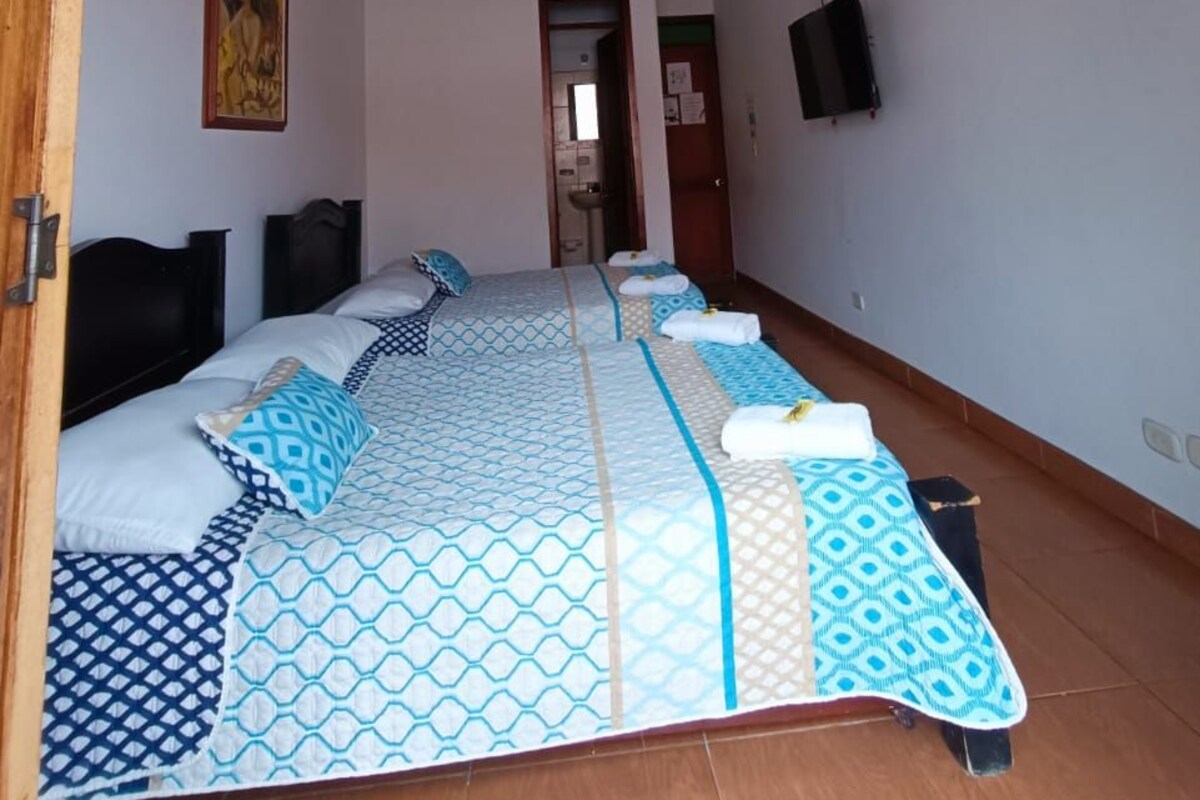 A room with a large bed, wooden ceiling beams, a painting on the wall, and a television.