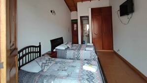 A bedroom with two beds, wooden ceiling beams, a TV mounted on the wall, and a door leading to another room. - Hotel Monte Verde (Salento)