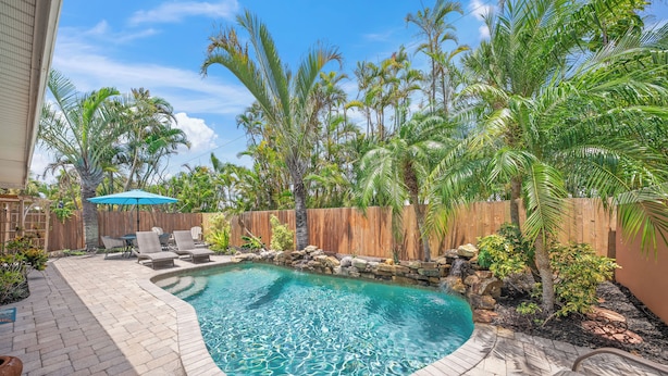 A backyard with a swimming pool, surrounded by palm trees and a wooden fence. - On Turtle Time - Beach Cottage w/ Heated Pool & Close to the Sand (Holmes Beach)