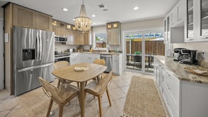 A modern kitchen with stainless steel appliances, wooden cabinets, and a dining area with wicker chairs. - On Turtle Time - Beach Cottage w/ Heated Pool & Close to the Sand (Holmes Beach)